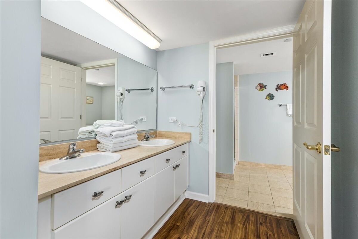 A bathroom with two sinks, a large mirror, and a walk-in shower.
