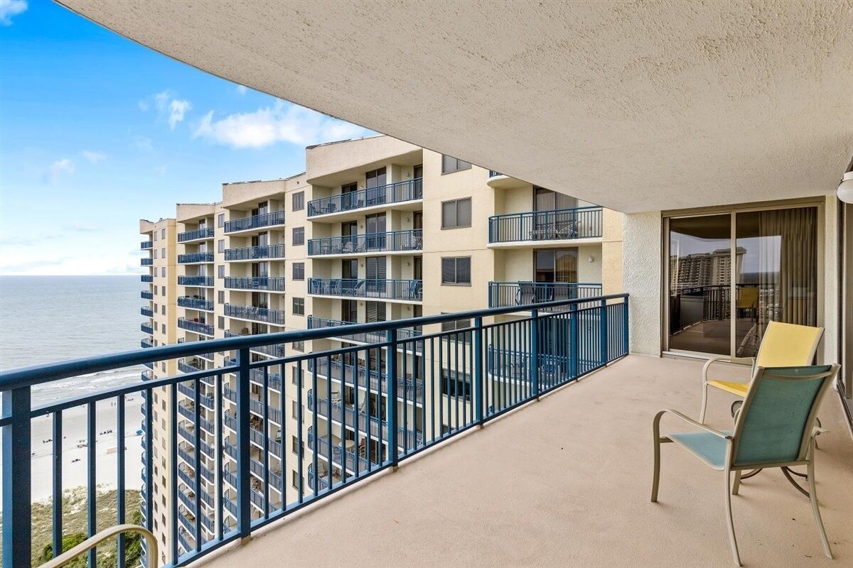 A balcony with a view of a beach and a multi-story building.