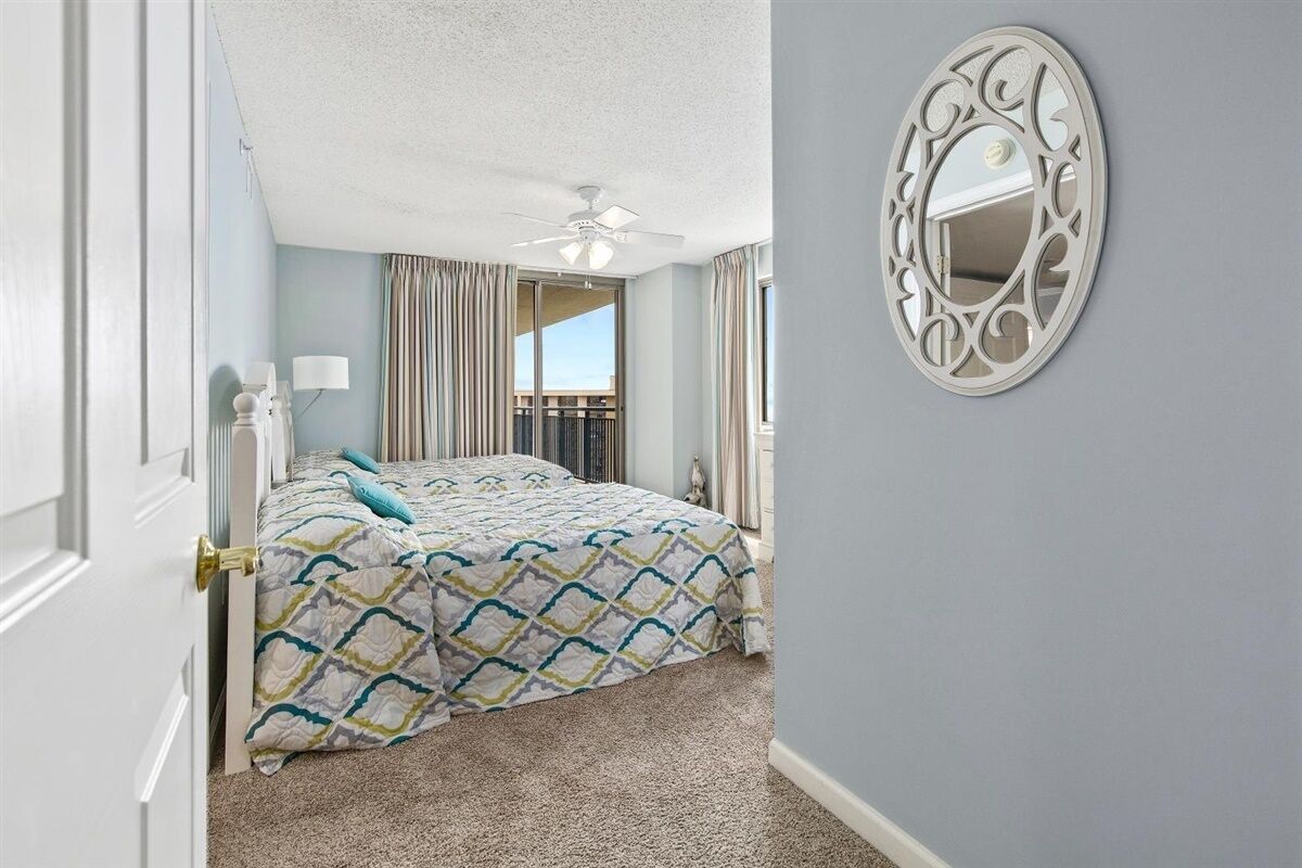 Une chambre à coucher avec un lit, un ventilateur de plafond, une fenêtre avec des rideaux et un miroir fixé au mur.