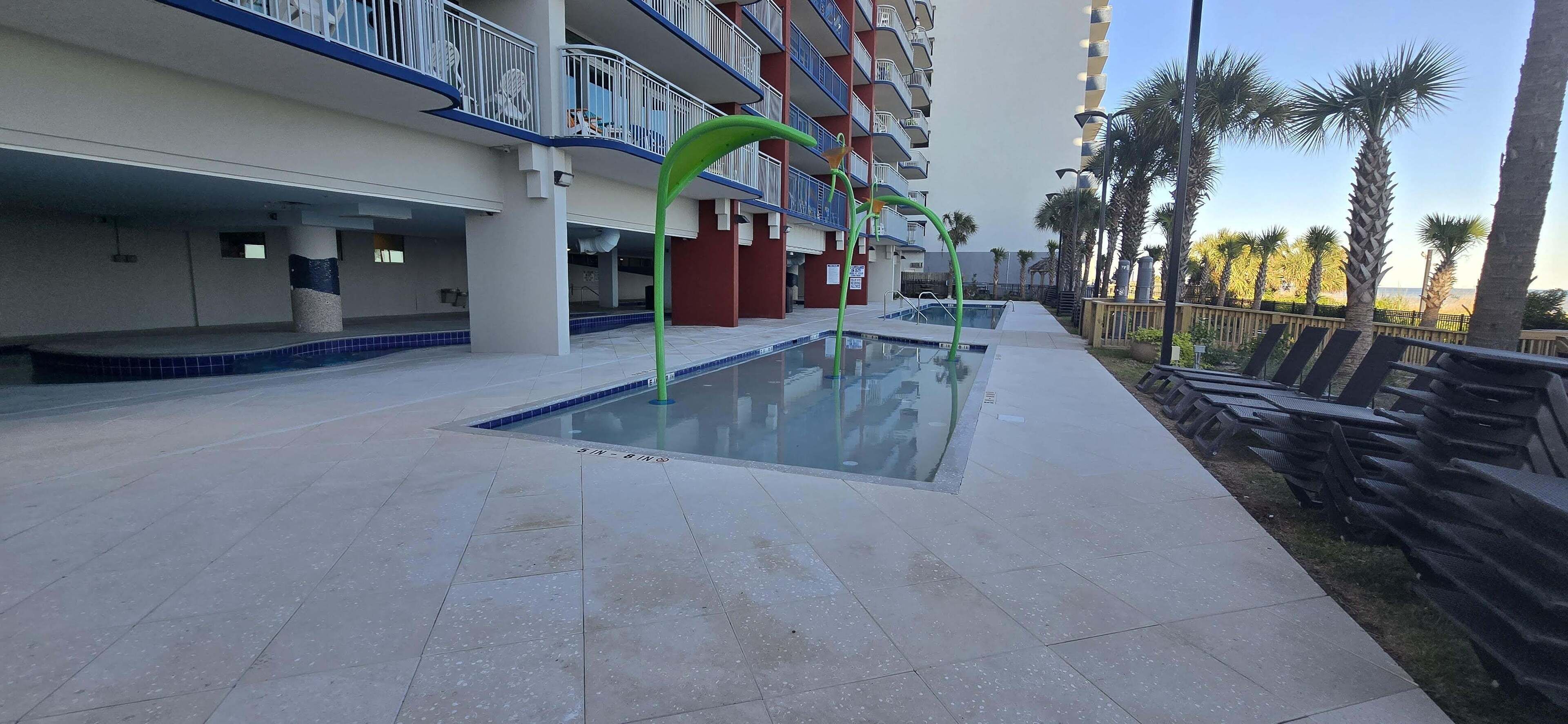 Un espace piscine d’hôtel offrant une vue dégagée sur le bassin, agrémenté d’une structure décorative verdoyante et d’une rangée de chaises longues disposées le long du bord de la piscine.