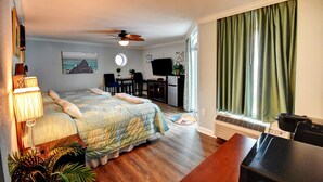 Ein Hotelzimmer mit einem Bett, einem Schreibtisch, einem Sessel, einem Fernseher und einem Vorhangfenster.