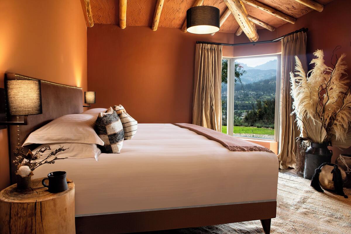 Un dormitorio con una cama grande, una mesita de noche con lámpara, una ventana con cortinas y vistas al exterior.