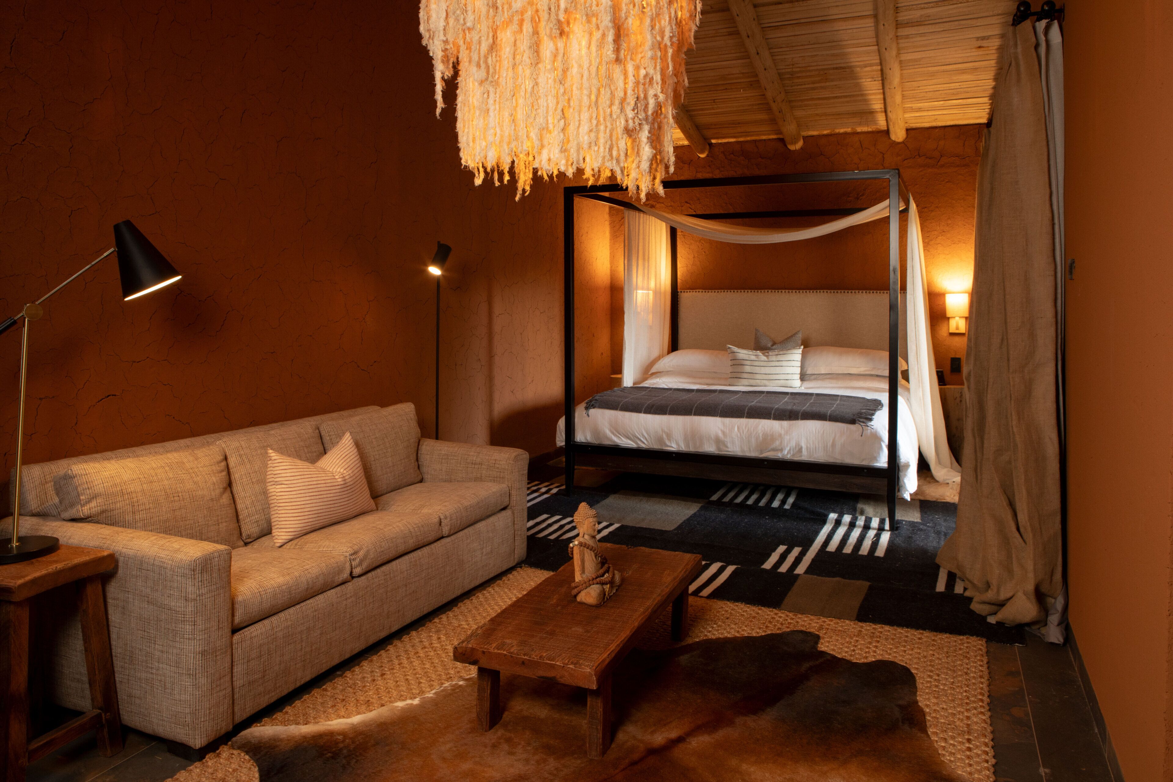 A bedroom with a four-poster bed, a sofa, a coffee table, and a hanging light fixture.