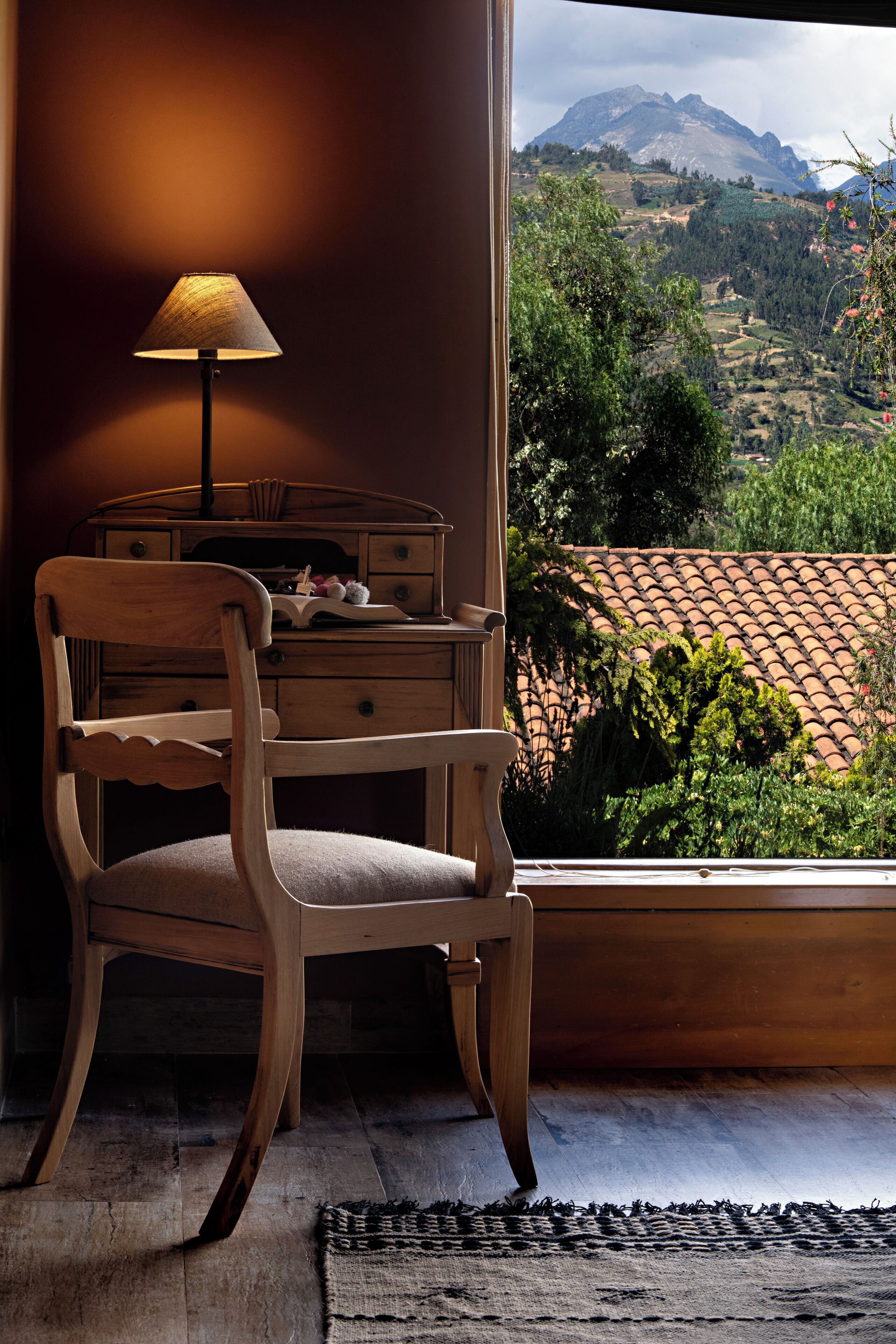 Ein Holzsessel mit einer Lampe neben einem Fenster mit Blick auf eine Berglandschaft.
