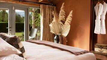 Un dormitorio con cama, una ventana con cortinas, un florero con plumas de pampa y un perchero con batas.