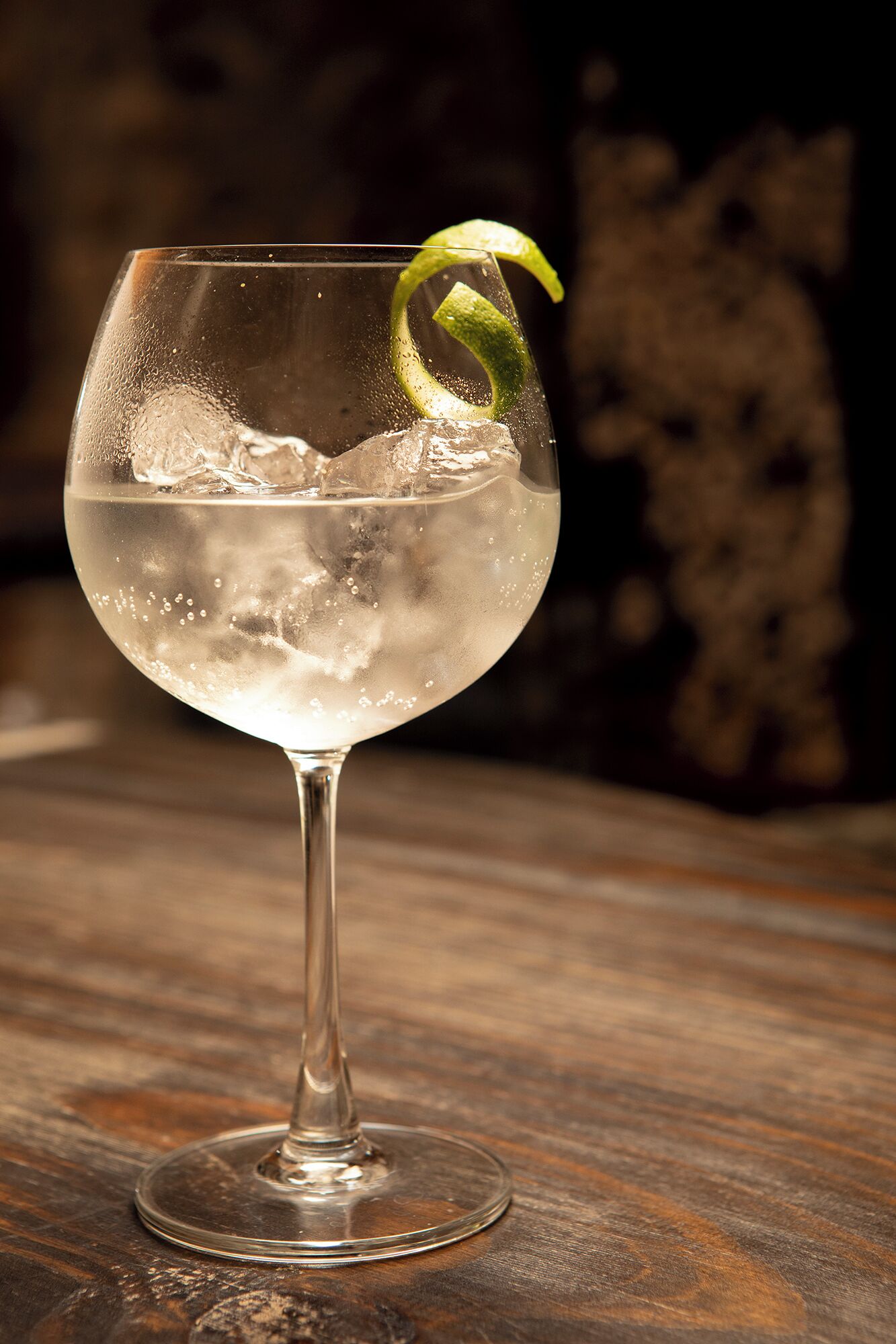 A glass of a clear, bubbly beverage with a lime garnish on a wooden surface.