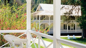 A gazebo with a white railing and a view of a house with a porch and a lawn.