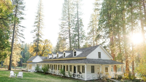 A white colonial-style house with a covered porch, surrounded by tall trees and a grassy yard.