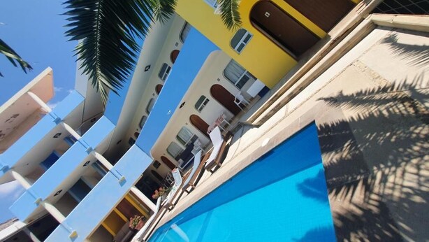 A multi-story hotel with balconies, a swimming pool, and palm trees. - Hotel Kootznoowoo (Puerto Escondido)