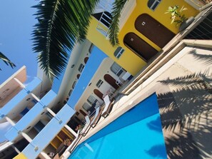 A multi-story hotel with balconies, a swimming pool, and palm trees. - Hotel Kootznoowoo (Puerto Escondido)