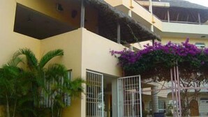A multi-story building with a yellow facade, a thatched roof, and a gated entrance. - Hotel Kootznoowoo (Puerto Escondido)