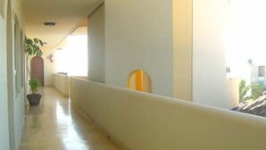 A corridor with a white wall, a wooden door at the end, and a potted plant. - Hotel Kootznoowoo (Puerto Escondido)