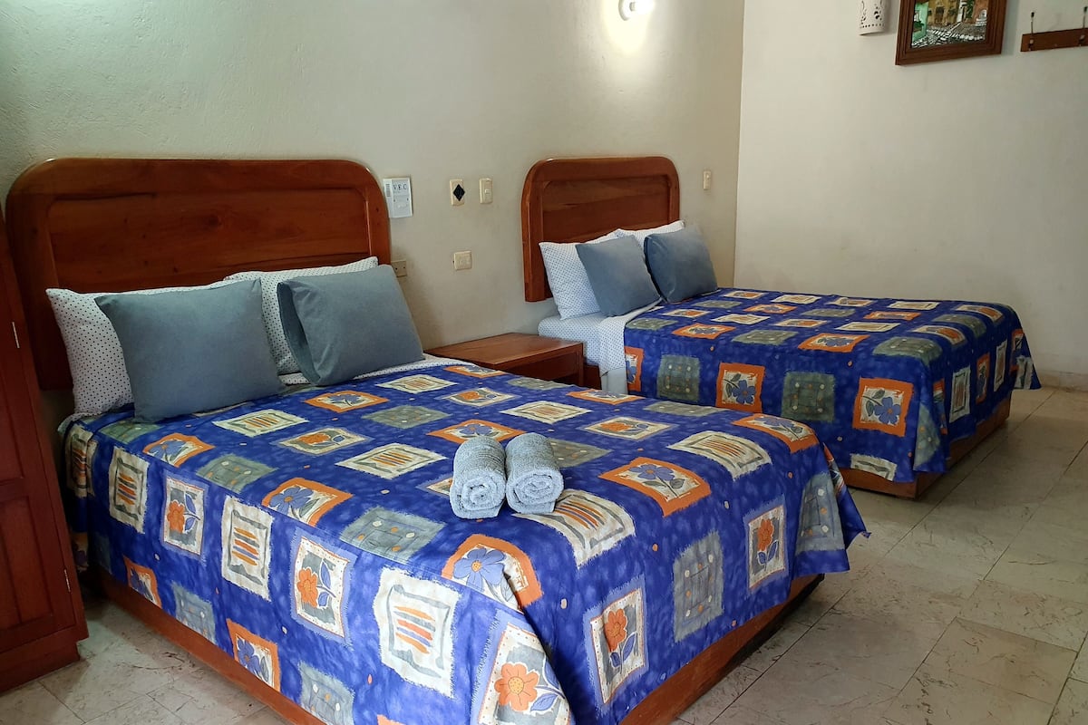 Two double beds with floral-patterned bedding, a wooden headboard, and a small bedside table with a lamp.