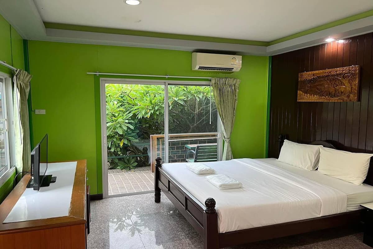 A hotel room with a bed, a desk with a computer, a window with curtains, and an air conditioning unit.