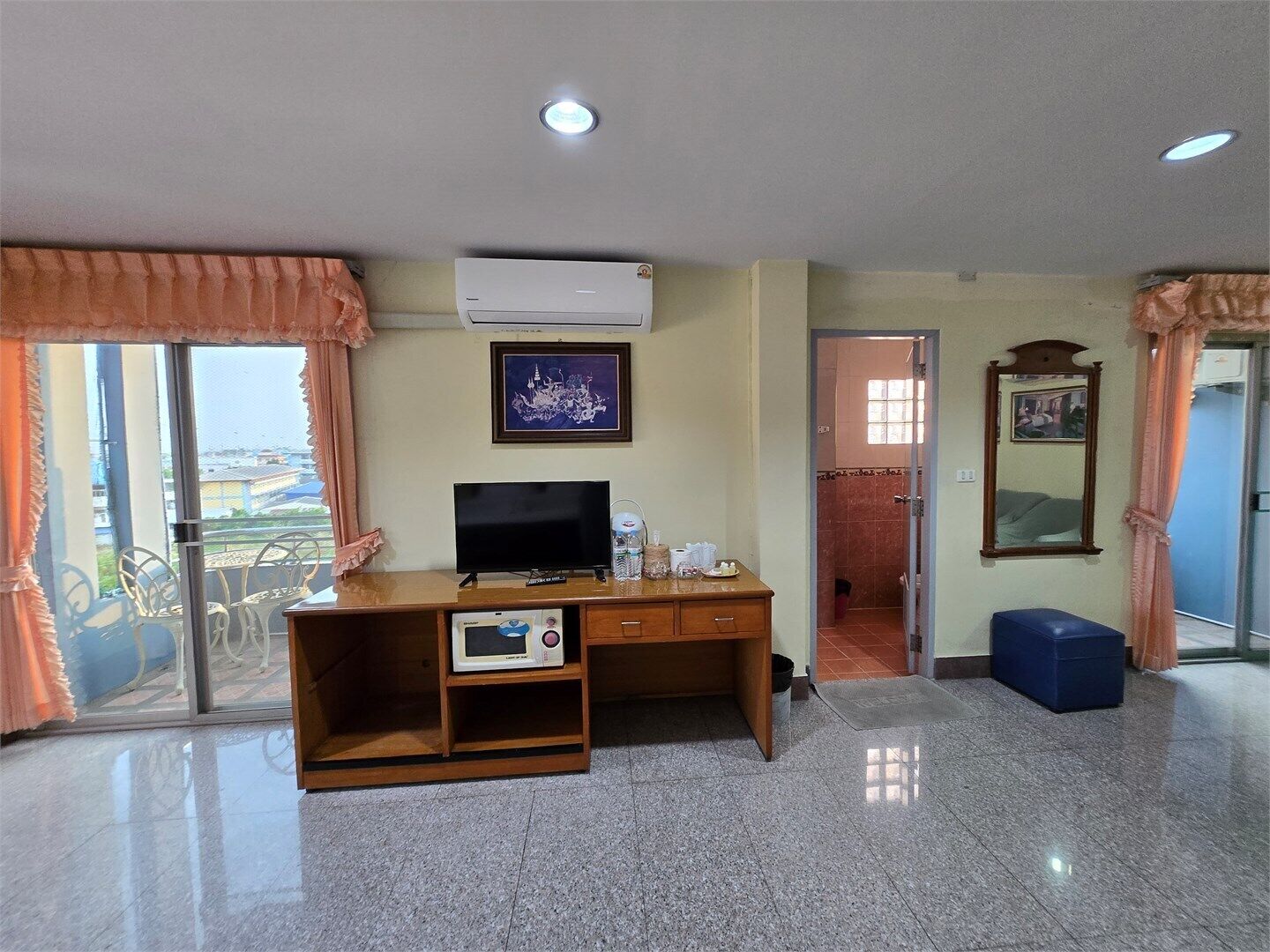 Quarto de hotel com secretária de madeira, televisão, quadro emoldurado e uma janela grande com cortinas.