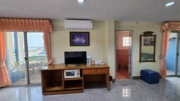 Quarto de hotel com secretária de madeira, televisão, quadro emoldurado e uma janela grande com cortinas.