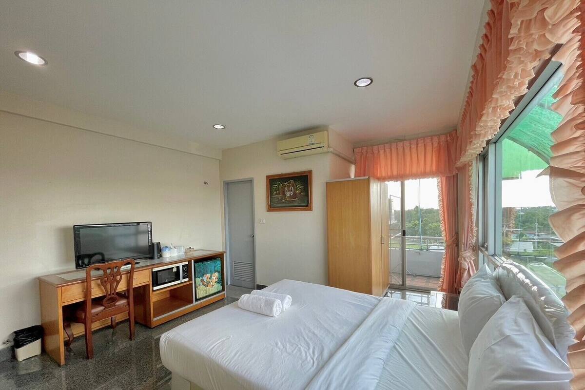 A hotel room with a bed, a desk with a television, a wardrobe, and a window with curtains.