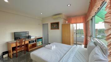 Quarto de hotel com cama, escrivaninha com televisão, guarda-roupa e janela com cortinas.