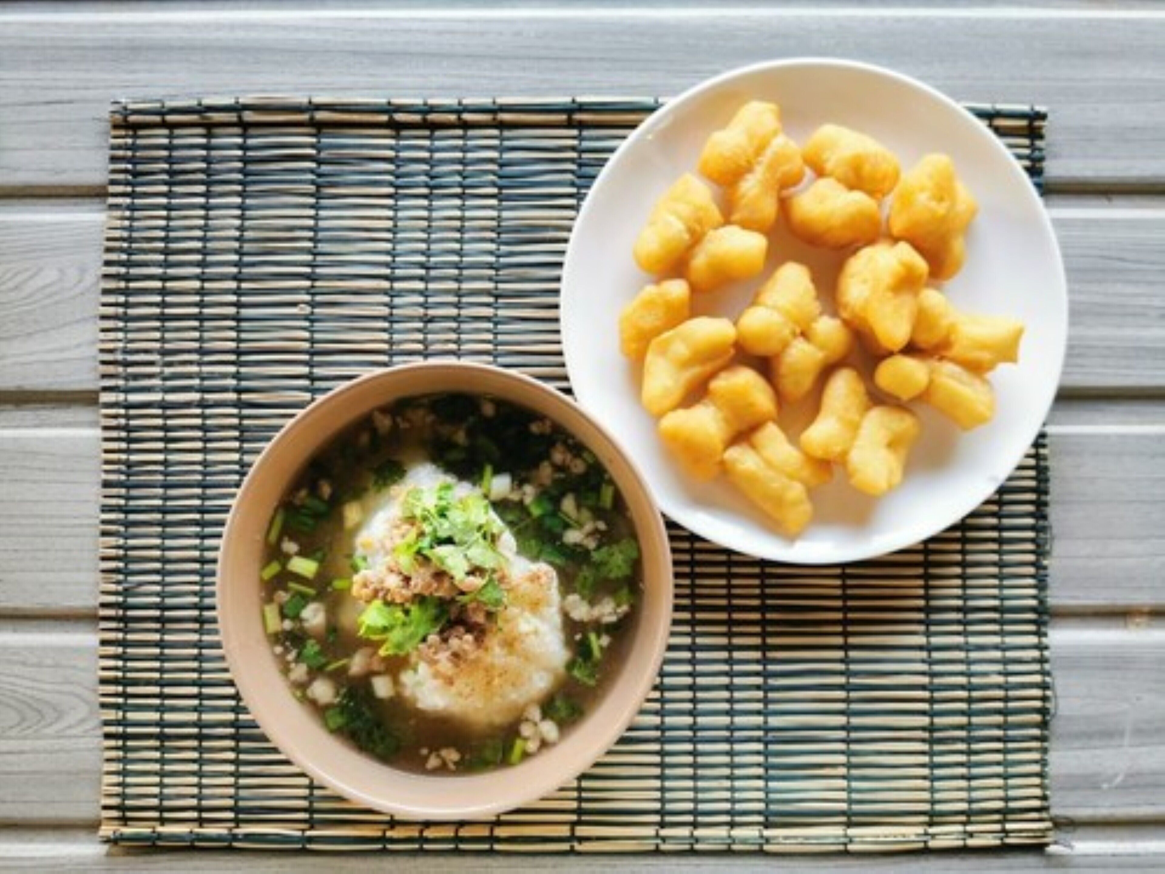 A bowl of soup with a fish and garnishes, and a plate of fried snacks on a bamboo mat.