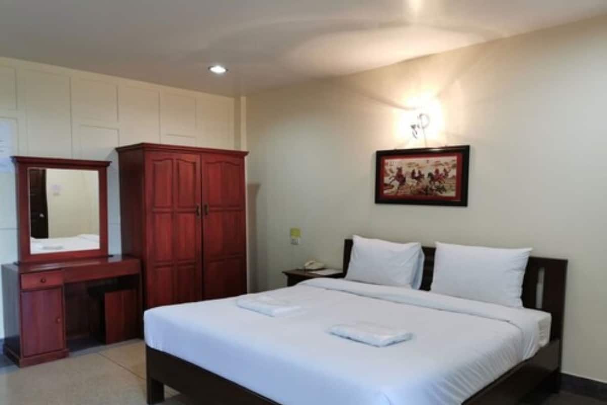 A hotel room with a bed, a wardrobe, a desk with a mirror, and a wall-mounted light fixture.