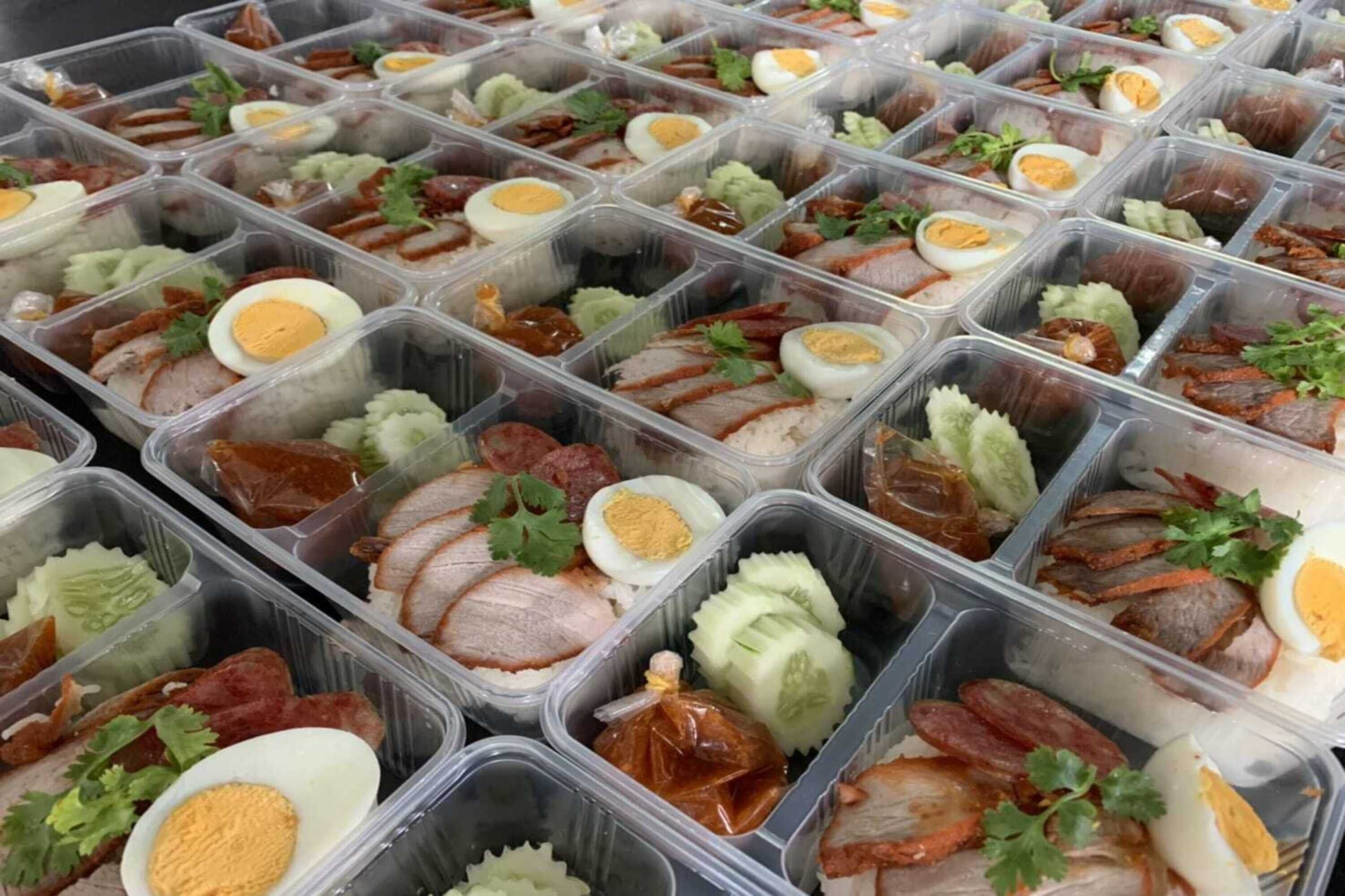 Multiple plastic containers filled with various food items, including sliced meat, boiled eggs, and garnishes.