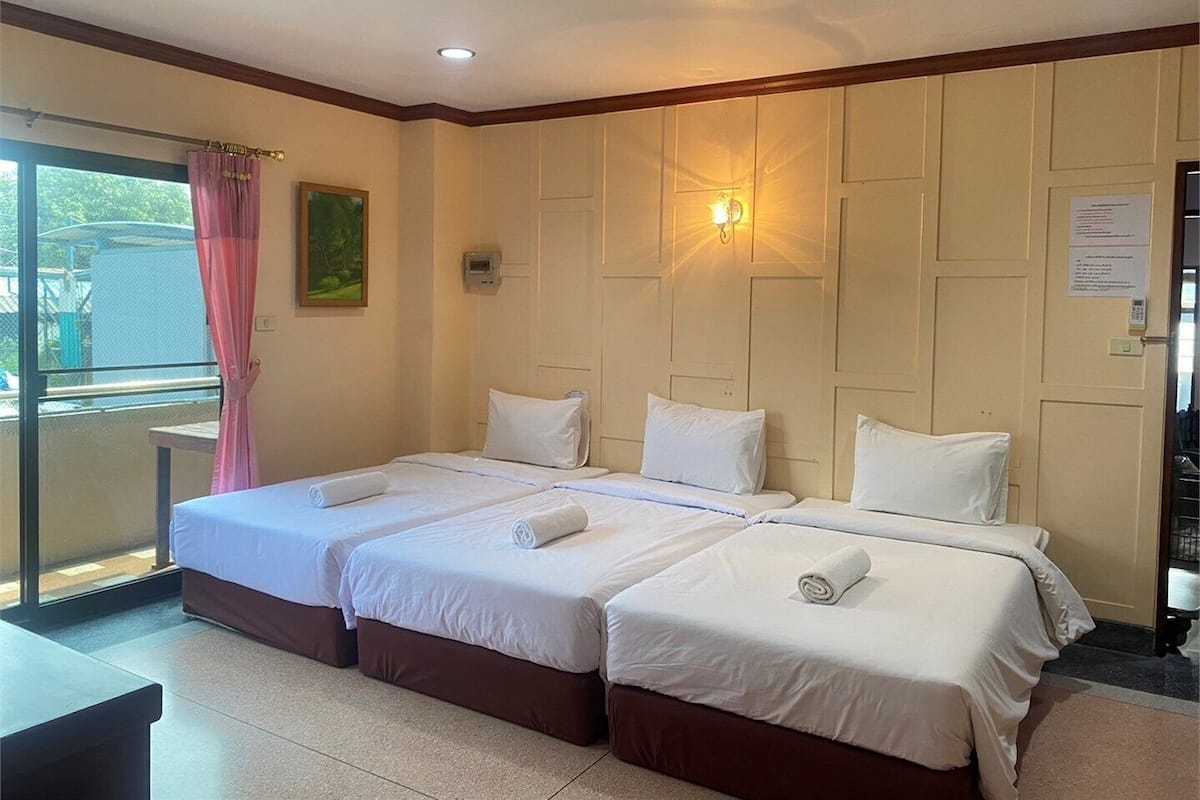 A hotel room with two beds, a balcony with a pink curtain, a wall-mounted light, and a small table.