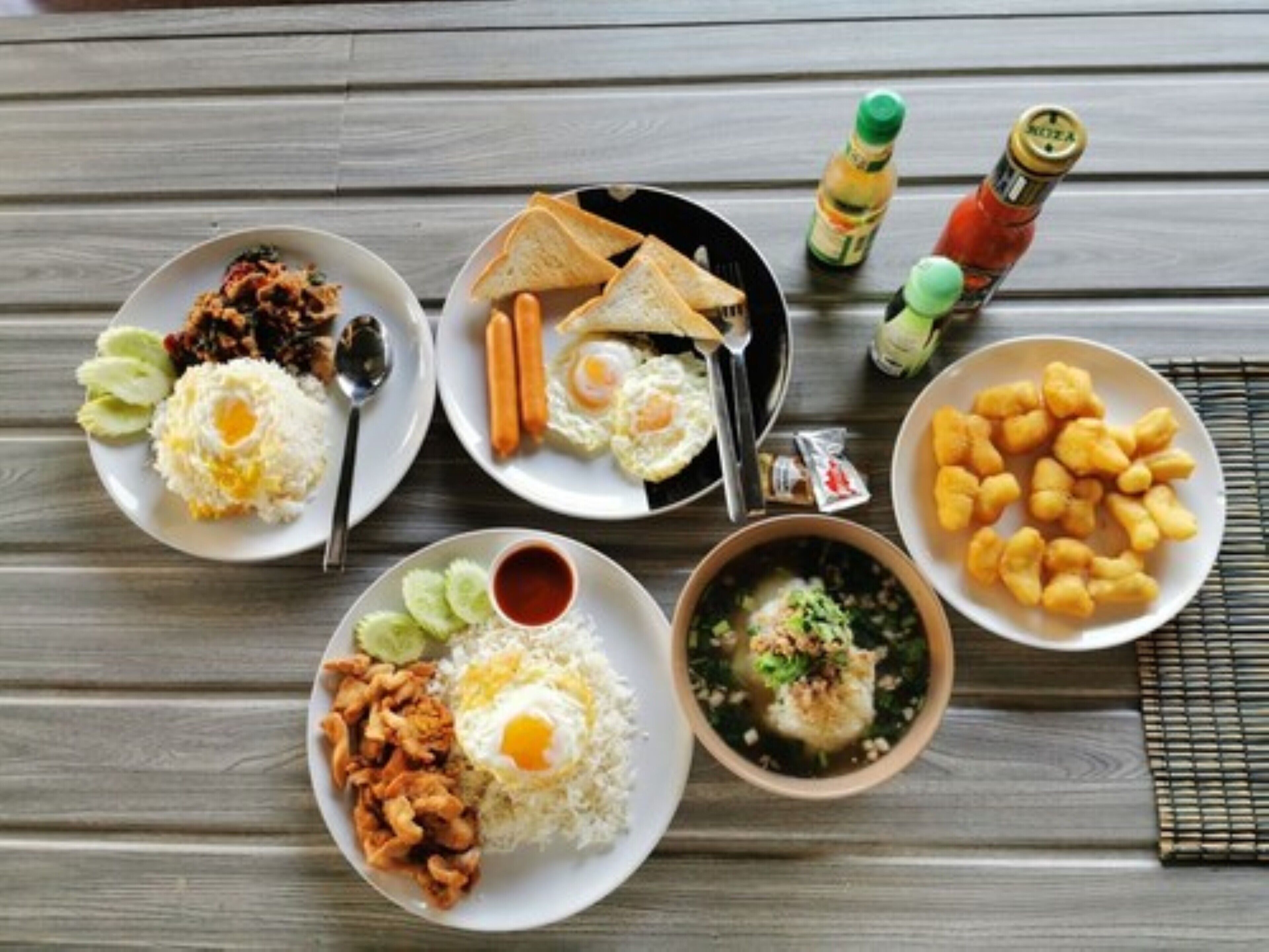 Una mesa con varios platos que incluyen arroz, huevos y frituras, junto con salsas y bebidas.