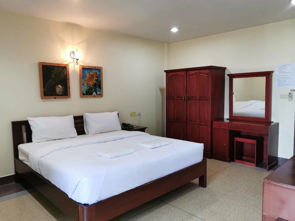 A hotel room with a large bed, a wooden wardrobe, a desk with a chair, and two wall-mounted paintings.
