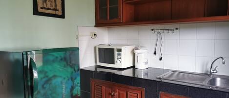 Une cuisine équipée d’un réfrigérateur, d’un four à micro-ondes, d’une bouilloire, d’un évier et de meubles de rangement en bois.