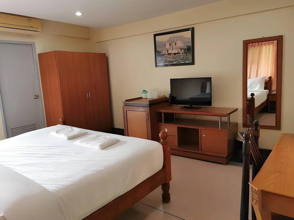 A hotel room with a bed, a television, a wardrobe, and a desk with a chair.