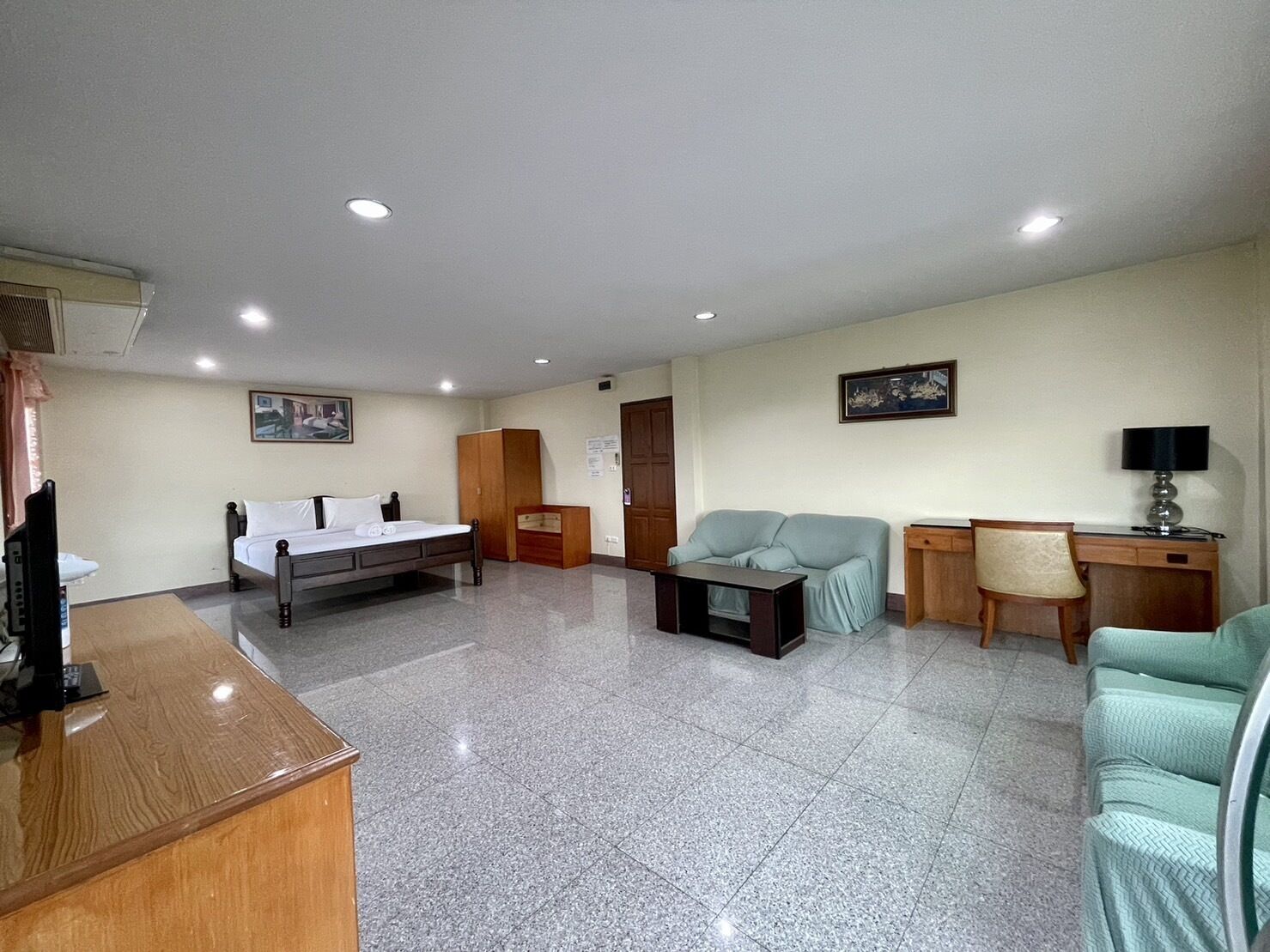 A hotel room with a bed, a desk, a chair, a sofa, and a television.