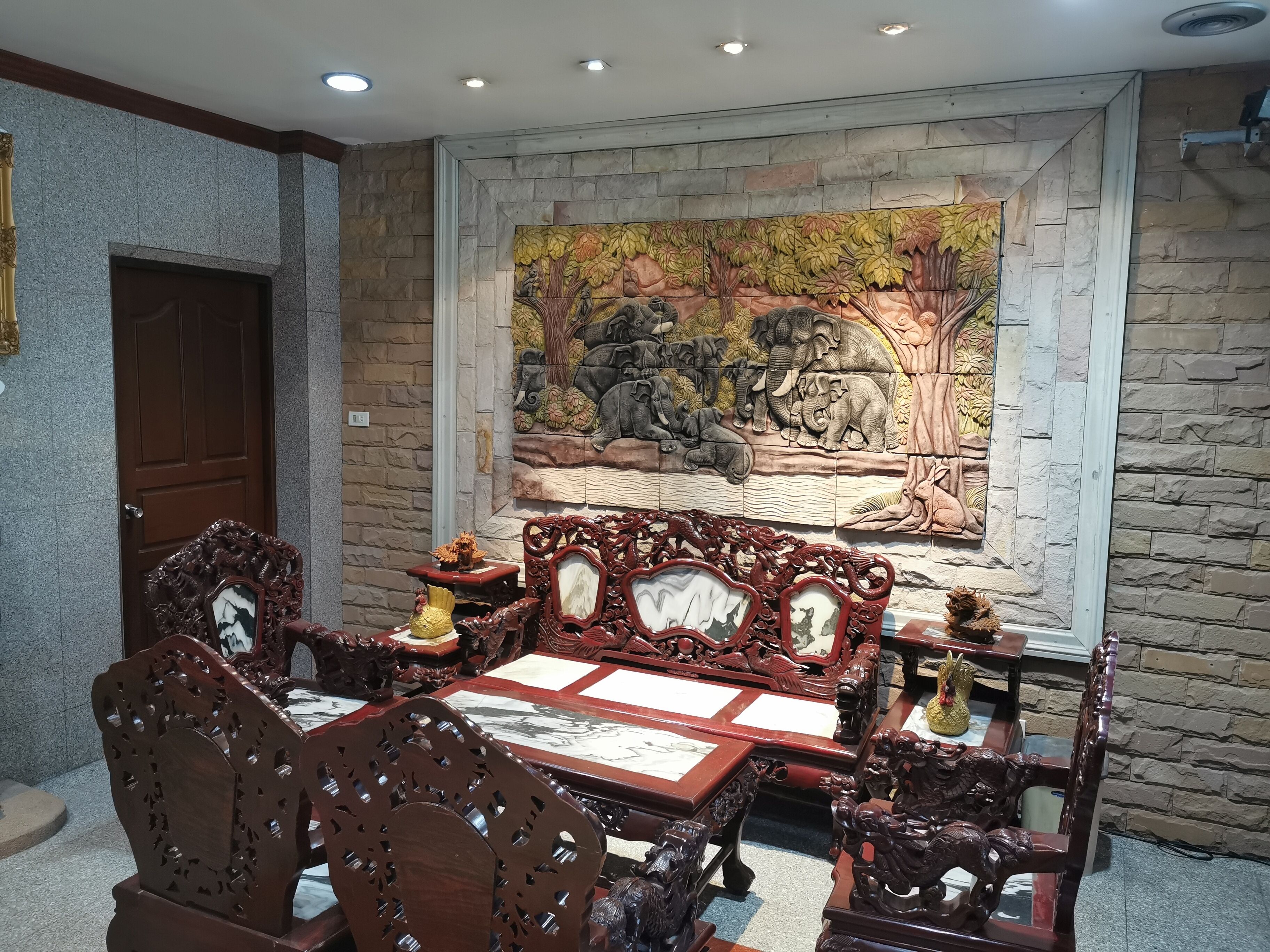 A traditional wooden dining table with ornate chairs, a stone wall with a mural, and a wooden door.