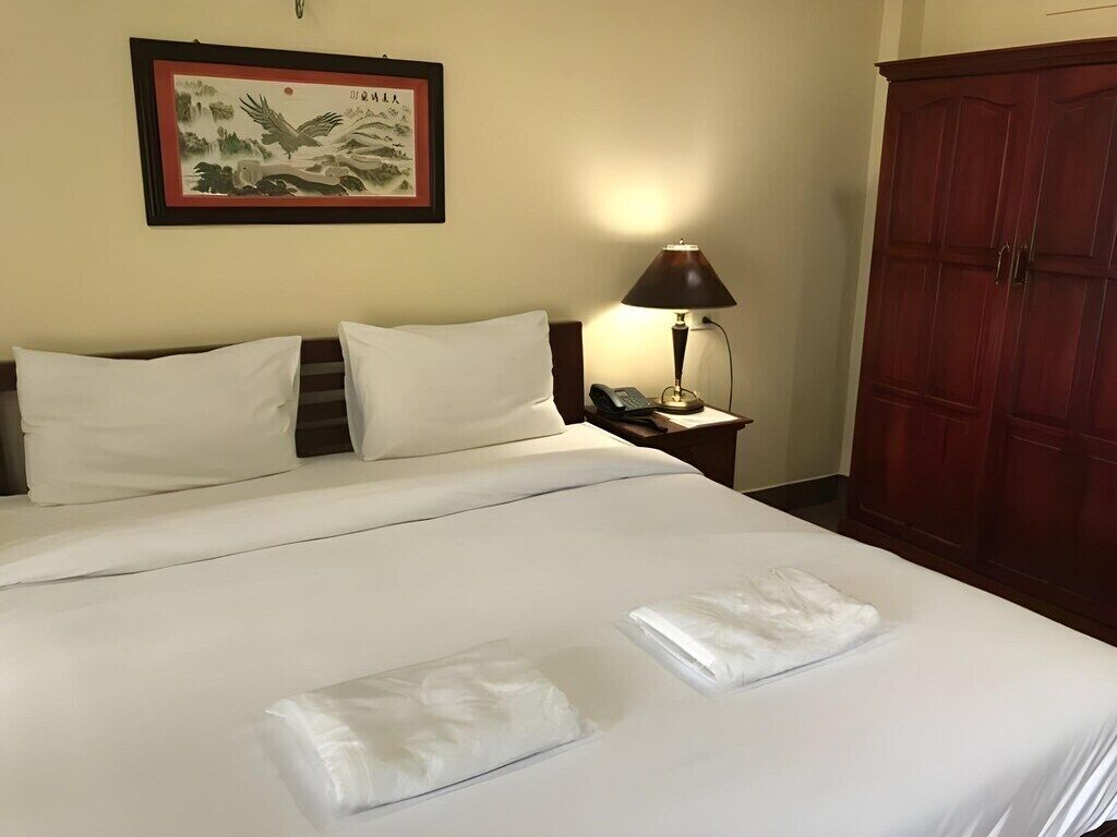 A hotel room with a bed, pillows, a bedside lamp, a telephone, and a wardrobe.