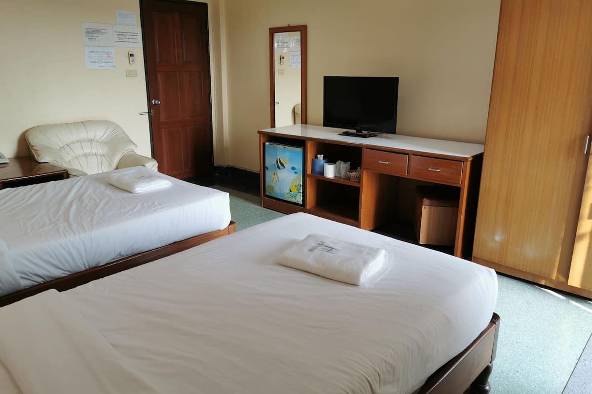 A hotel room with two beds, a desk with a television, a chair, a wardrobe, and a small cabinet.