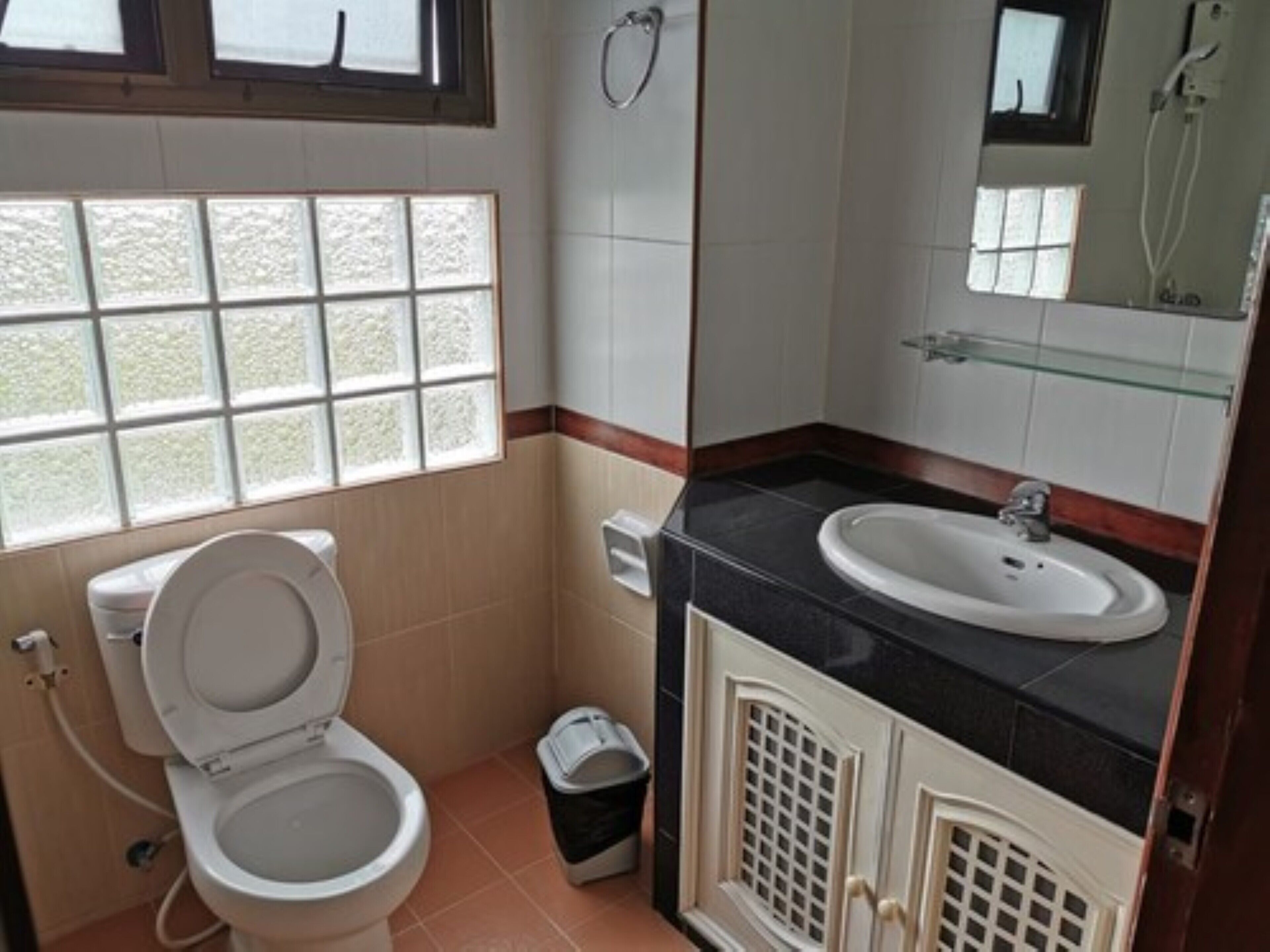 Une salle de bain avec des toilettes, un lavabo et une douche. Il y a une fenêtre au-dessus des toilettes et un miroir au-dessus du lavabo.