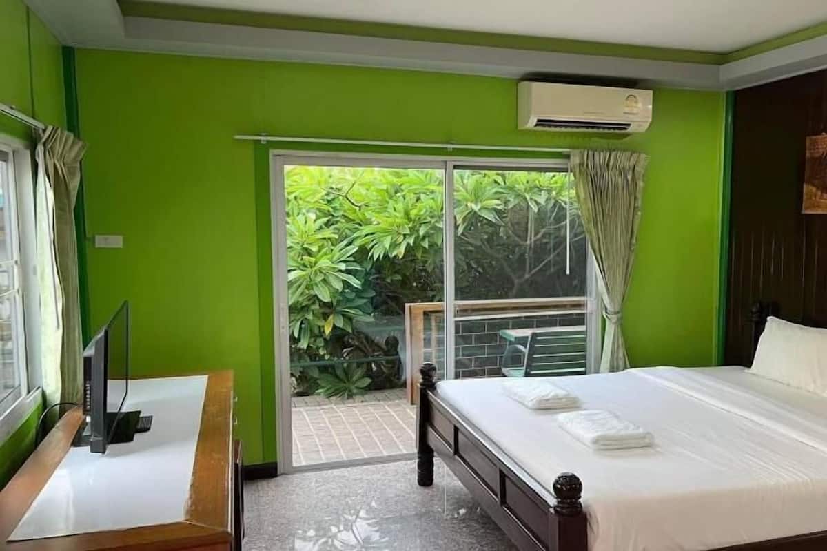 A hotel room with a bed, a TV, a window with curtains, and an air conditioning unit.