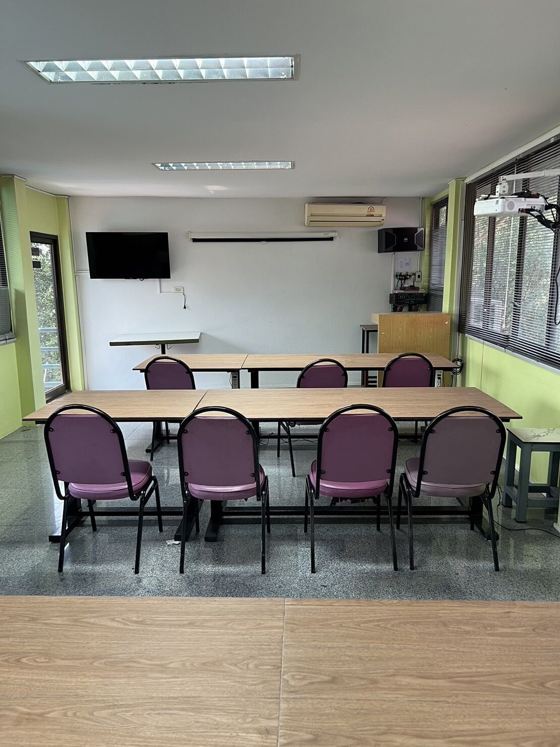 Un salón de conferencias con una larga mesa, seis sillas, un televisor de pantalla plana, un equipo de aire acondicionado y un proyector.
