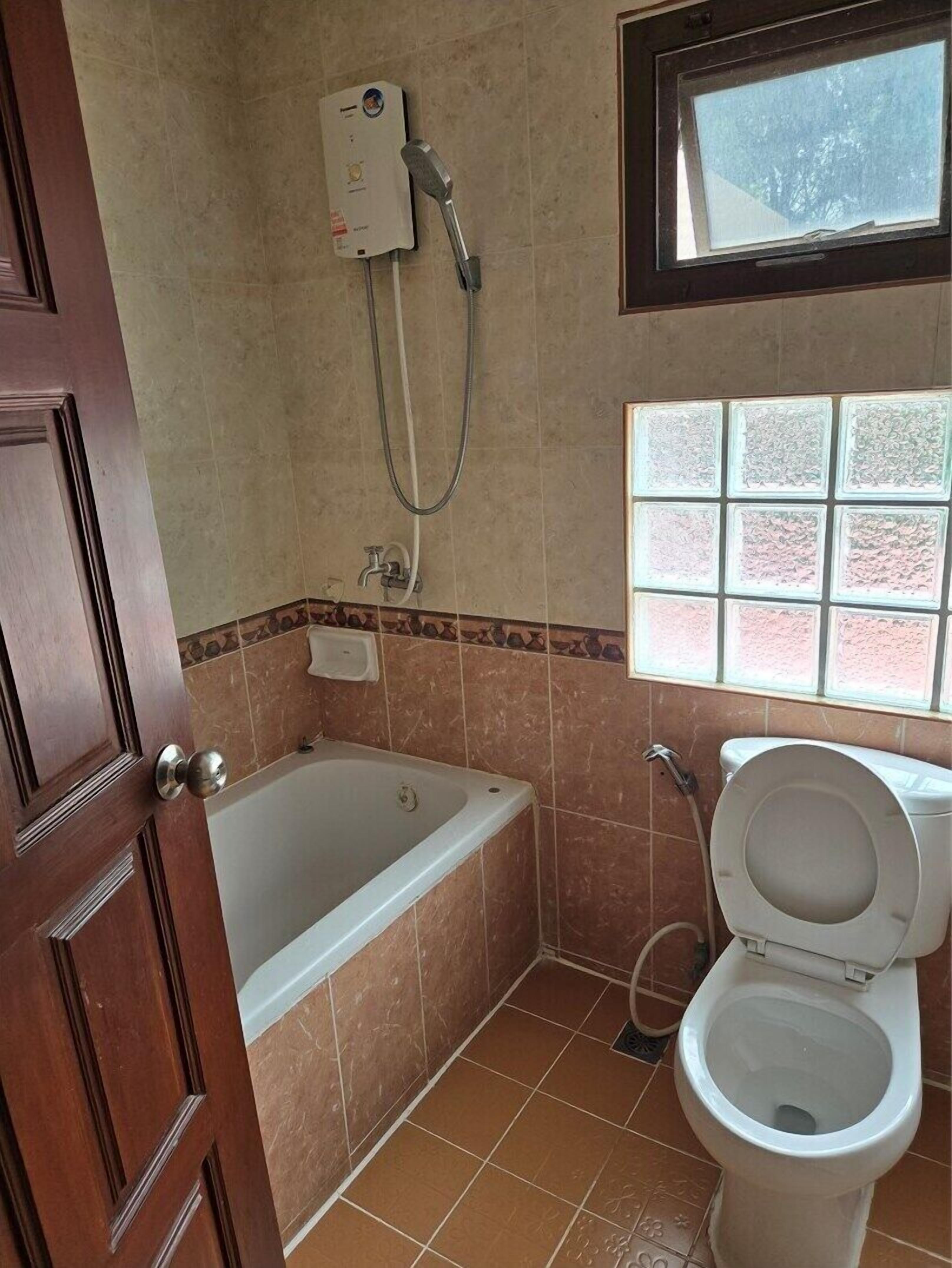 Un baño con bañera, inodoro y ventana con vistas a árboles.