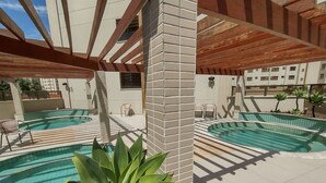 A rooftop pool area with two swimming pools, lounge chairs, and a large plant.