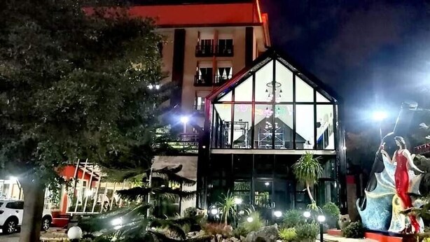 Un bâtiment doté d’une façade en verre et d’un balcon, entouré d’arbres et éclairé par des lampadaires.