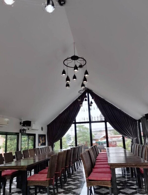 Une salle de conférence dotée de longues tables et de chaises, d’un lustre moderne et de grandes fenêtres avec des rideaux.