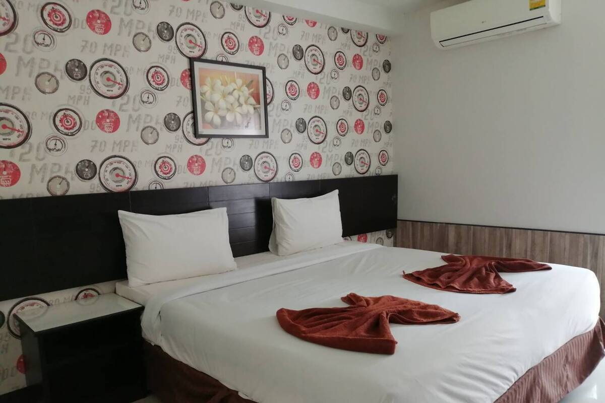 A hotel room with a bed, white bedding, a headboard, a nightstand, and a wall with a speedometer pattern.