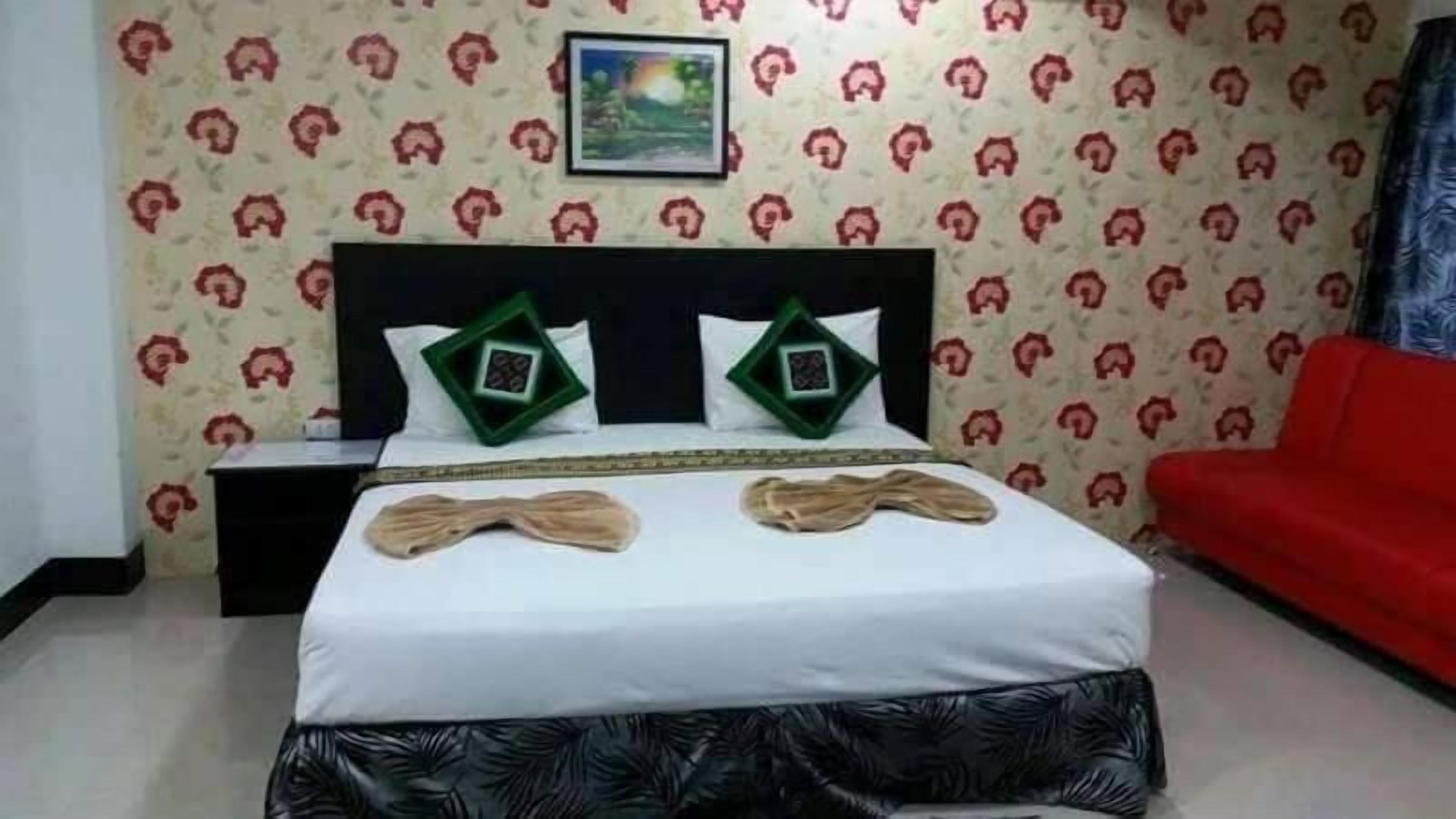 A neatly made bed with a white sheet and two green pillows, a red sofa, and a nightstand with a green tray.