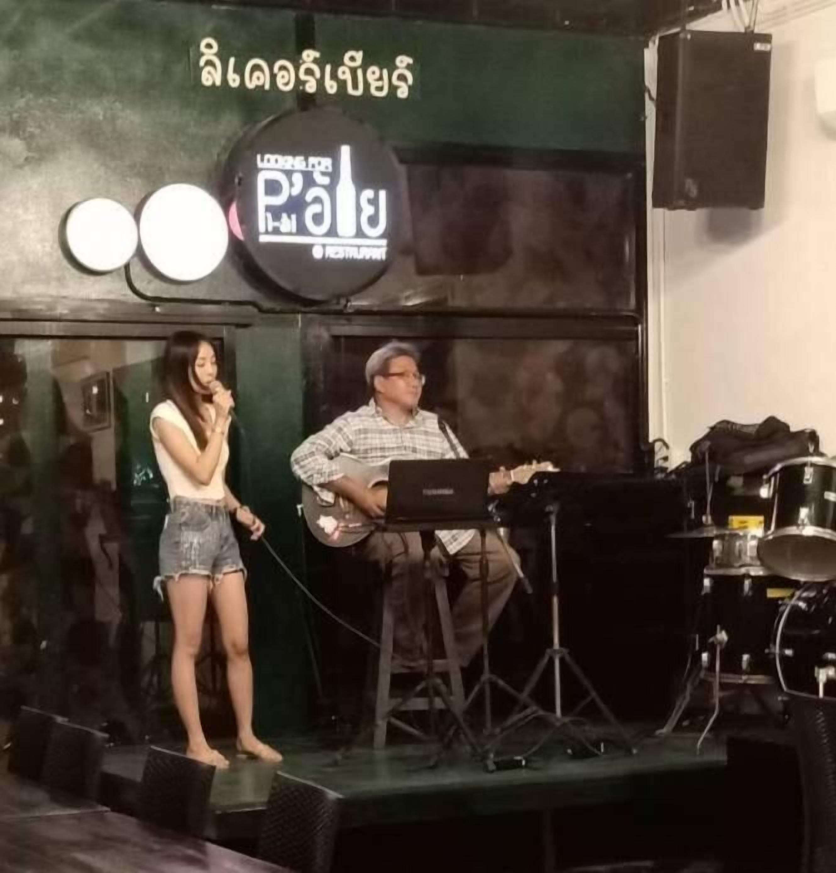 Un escenario con un soporte para micrófono y una guitarra, una computadora portátil y un altavoz sobre una mesa.