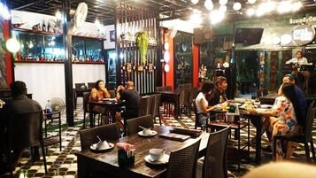 A restaurant with multiple tables and chairs, a bar area with bottles and glasses, and a ceiling with hanging lights.