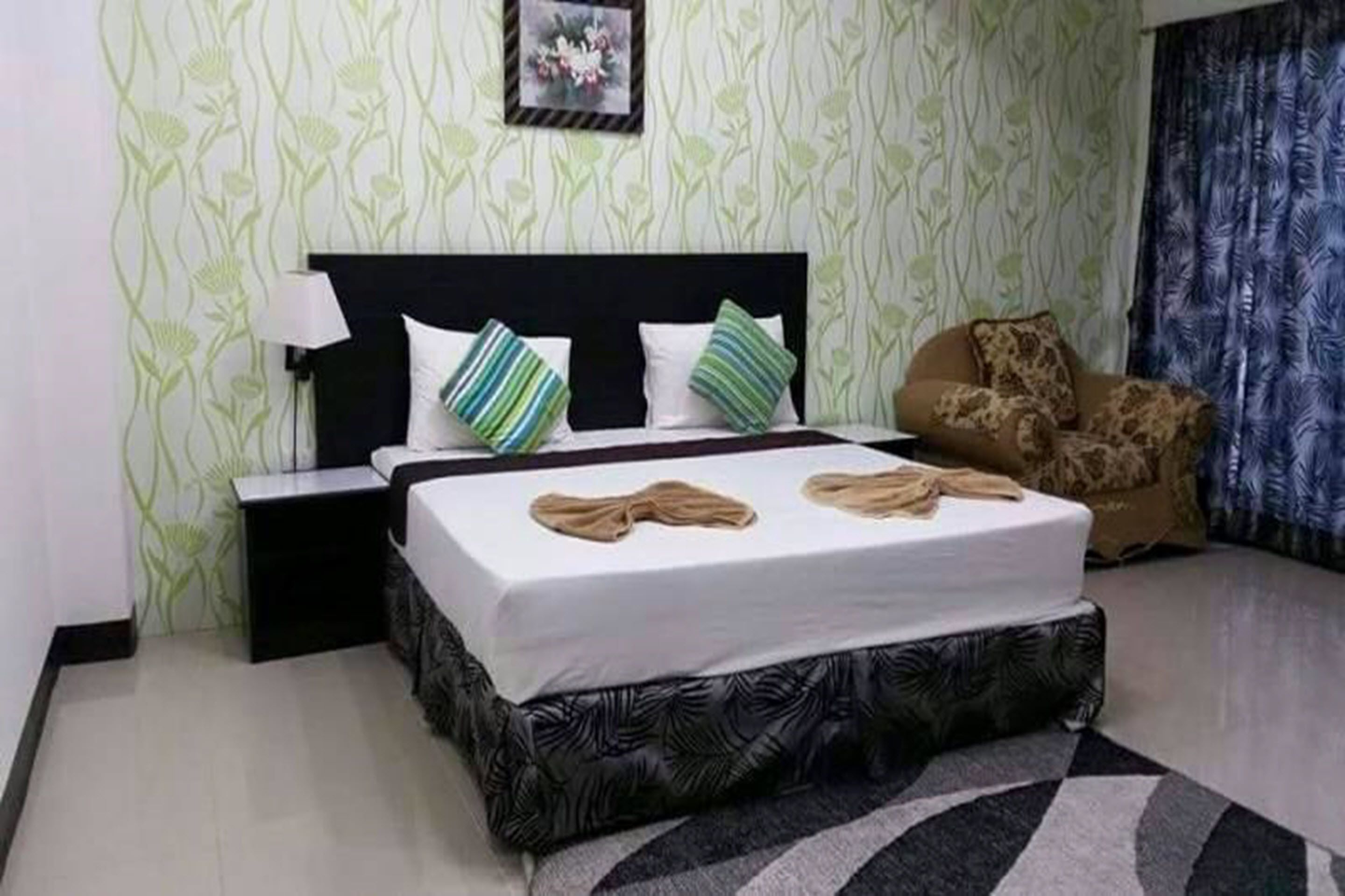 A neatly arranged bedroom with a bed, a nightstand, a chair, and a patterned wall.