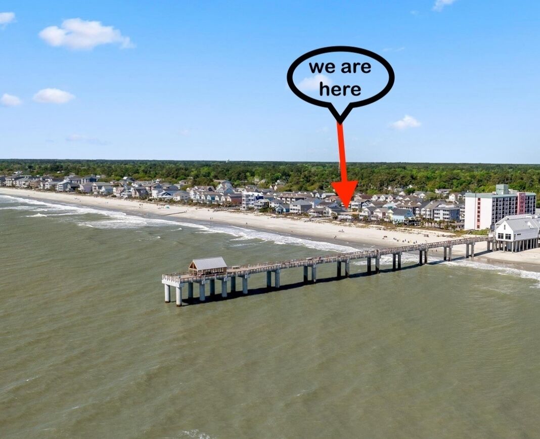 An aerial view of a coastal town with a pier extending into the water, a beach, and residential buildings.