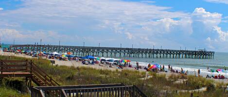A pier extending into the water with a beach area in the foreground.