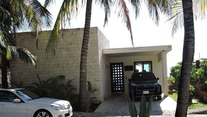A two-story building with a paved driveway, a white car parked on the left, and a black car parked in the garage. - Casa Moskito, Oceanfront beautiful Villa, 150 Mbps (Playa del Carmen)