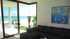 A modern living room with a large sectional sofa, a glass coffee table, and a view of the ocean through large sliding glass doors. - Casa Moskito, Oceanfront beautiful Villa, 150 Mbps (Playa del Carmen)